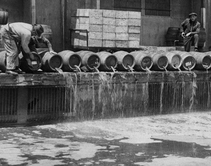 Рабочие (слева) выливают пиво на землю. Вооруженный сотрудник (справа) наблюдает за процессом. Brooklyn Army Base, 1925 год 